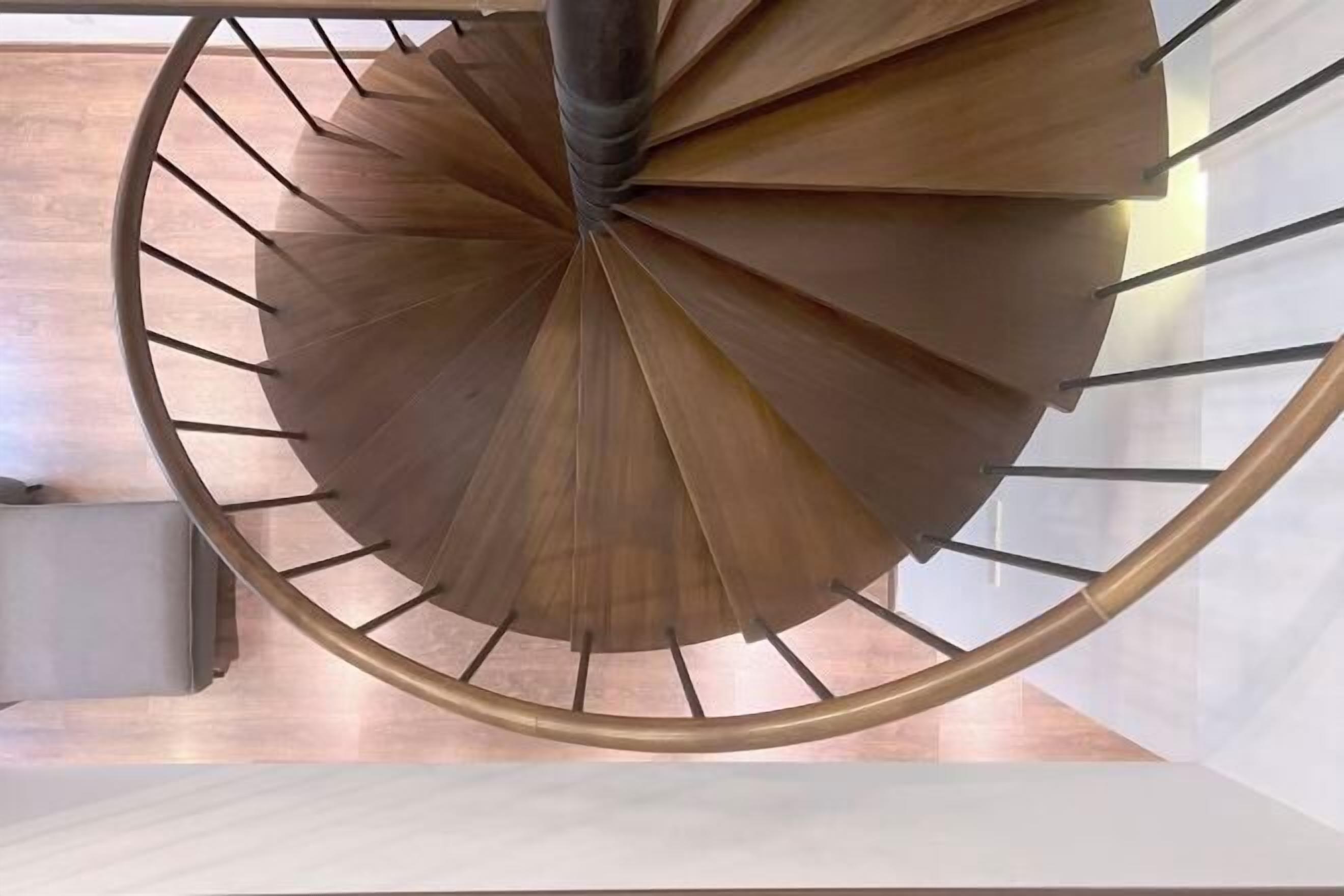 A spiral staircase with a metallic handrail and wooden steps.