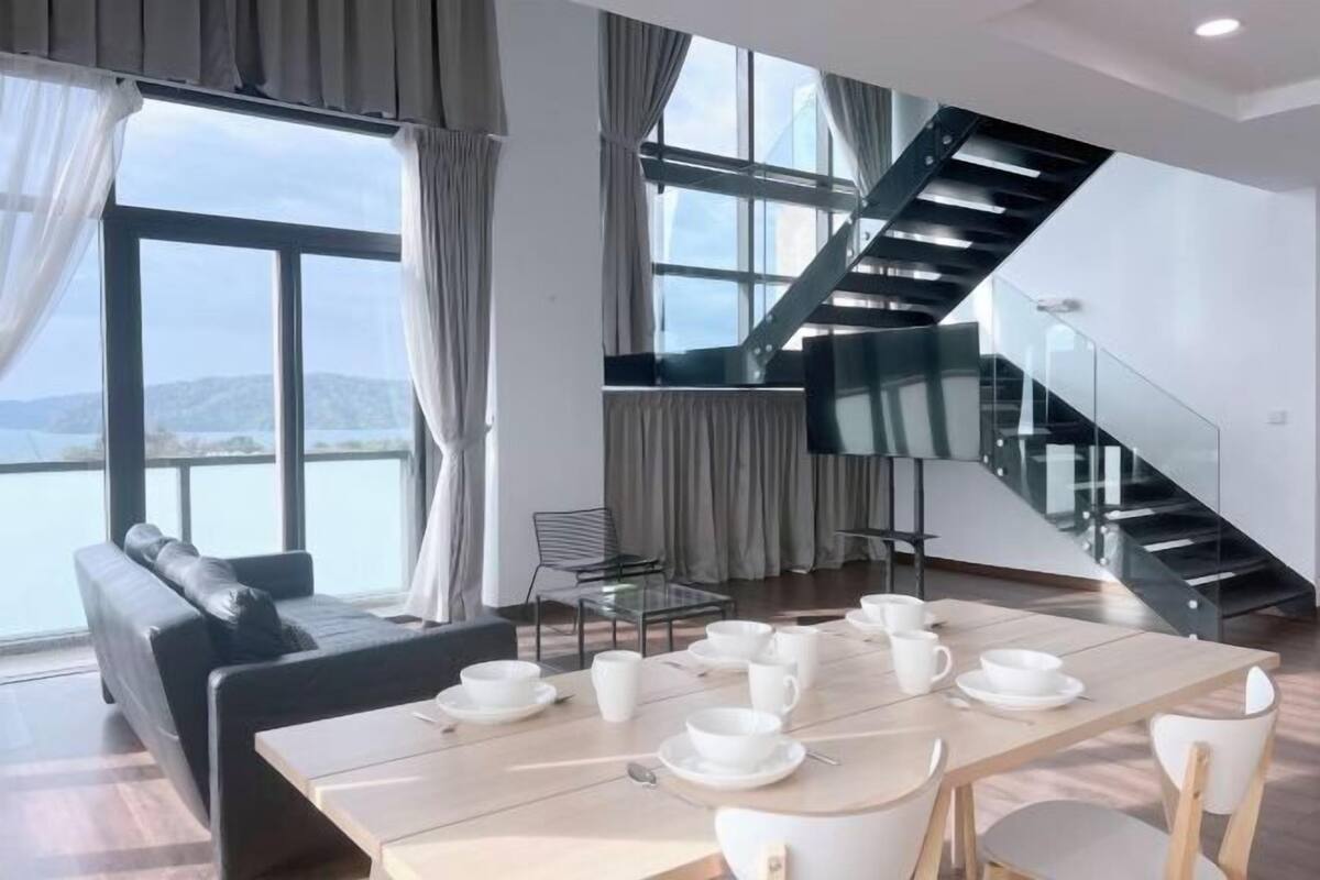 Una habitación moderna con una mesa de comedor preparada para té, una escalera negra y vista al mar.
