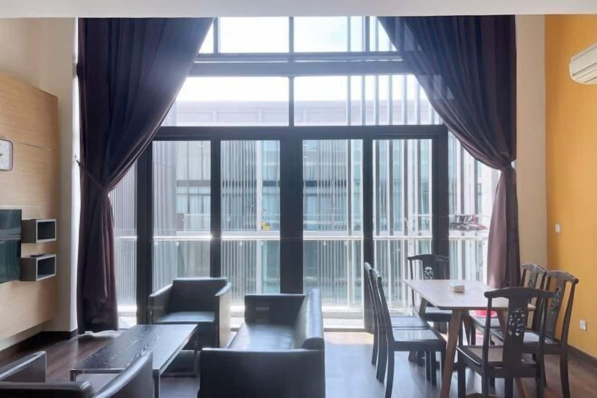 Ein modernes Hotelzimmer mit großem Fenster, einem Essbereich mit Tisch und Stühlen sowie einem an der Wand befestigten Fernseher.