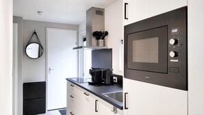 Moderni keittiö, jossa on sisäänrakennettu mikroaaltouuni, kahvinkeitin ja vedenkeitin työtasolla.