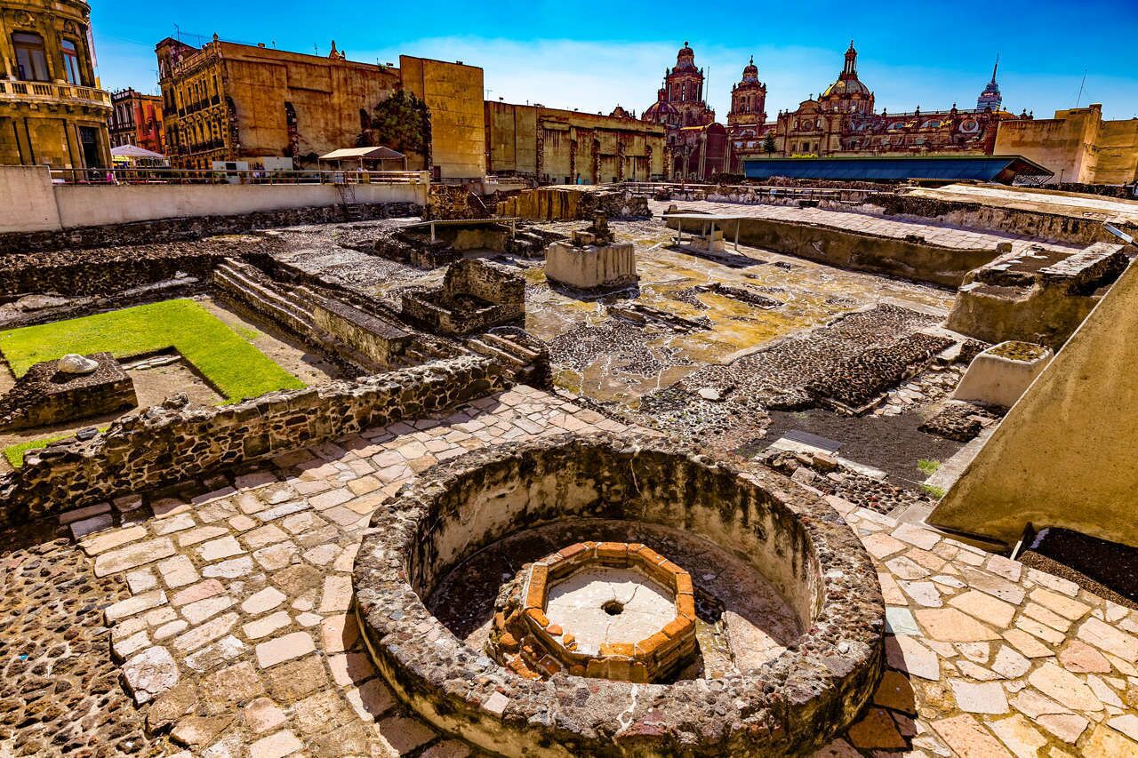 Un antiguo sitio arqueológico con estructuras de piedra y ruinas, que incluye un pozo circular y un patio rectangular.