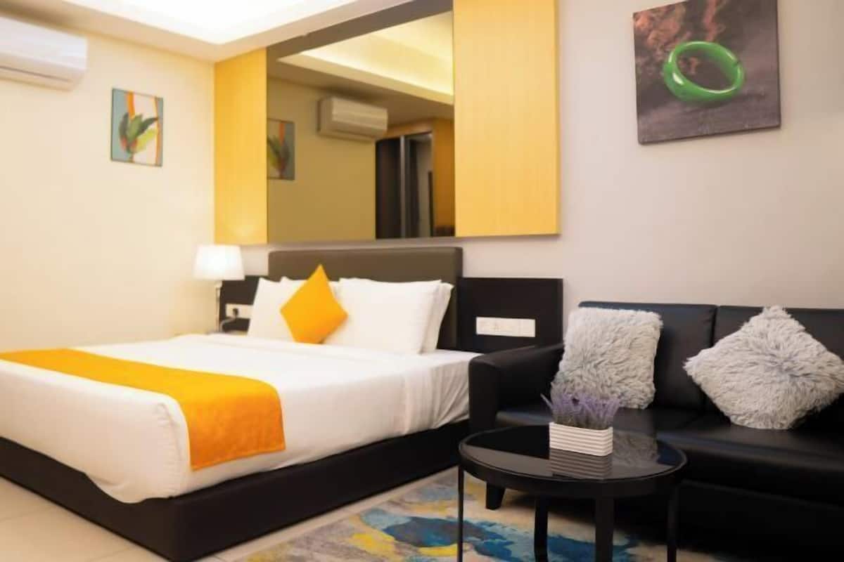 Una camera d'albergo con un letto, un divano nero, un tavolino e uno specchio appeso al muro.