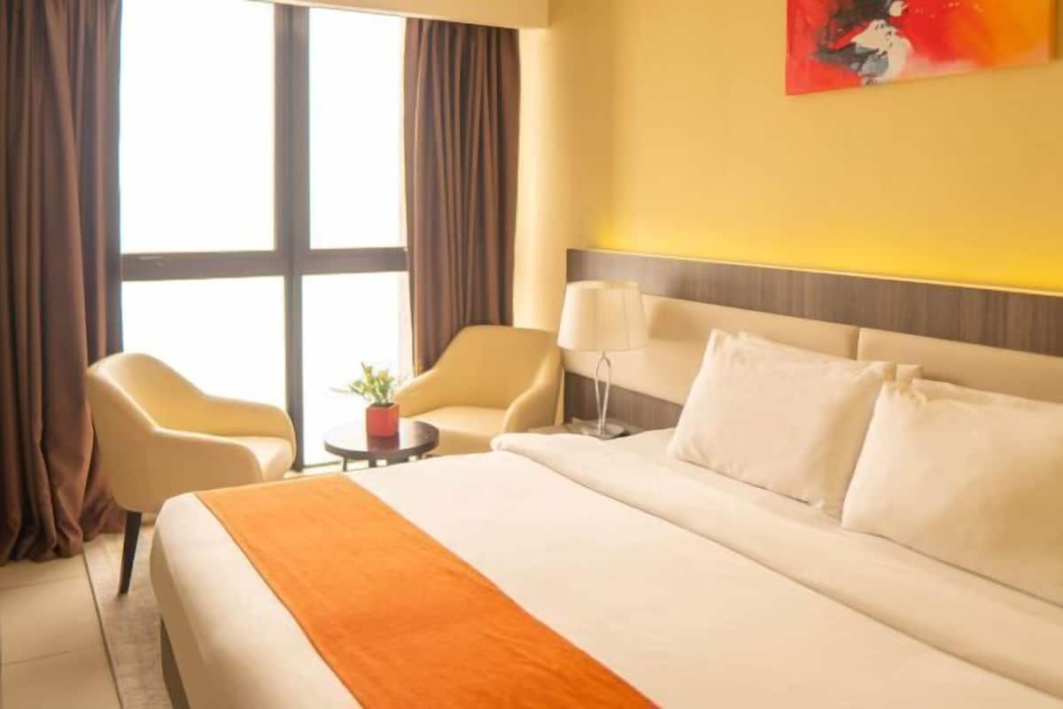 Camera d'albergo con un letto grande, due poltrone, un tavolino con una lampada e una finestra con tende.