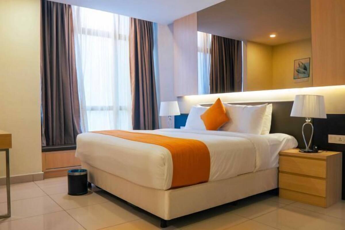 Una camera d'albergo con un letto grande, due comodini, una finestra con tende e una lampada a parete.