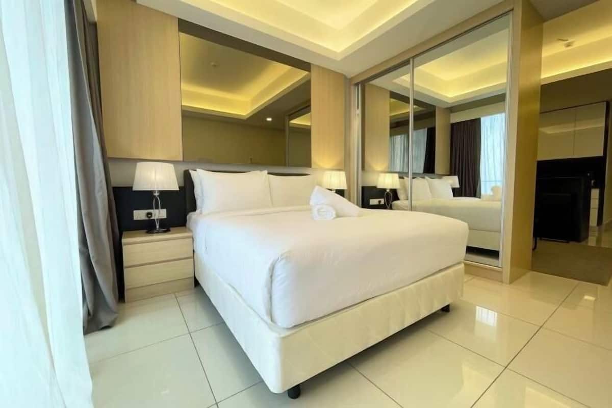Camera d'hotel moderna con un grande letto, comodini con lampade, uno specchio ampio e una porta scorrevole che dà accesso a un'altra stanza.