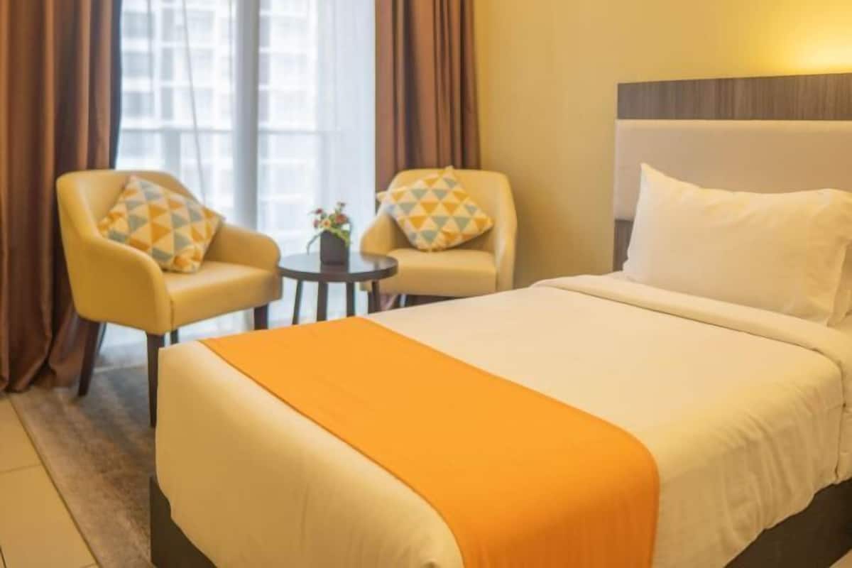Una camera d'albergo con un letto, due poltrone, un tavolino e una finestra con tende.