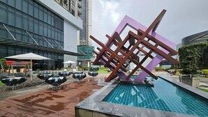 Une piscine extérieure agrémentée d’une sculpture géométrique moderne, entourée d’espaces de détente et avec un bâtiment visible en arrière-plan.