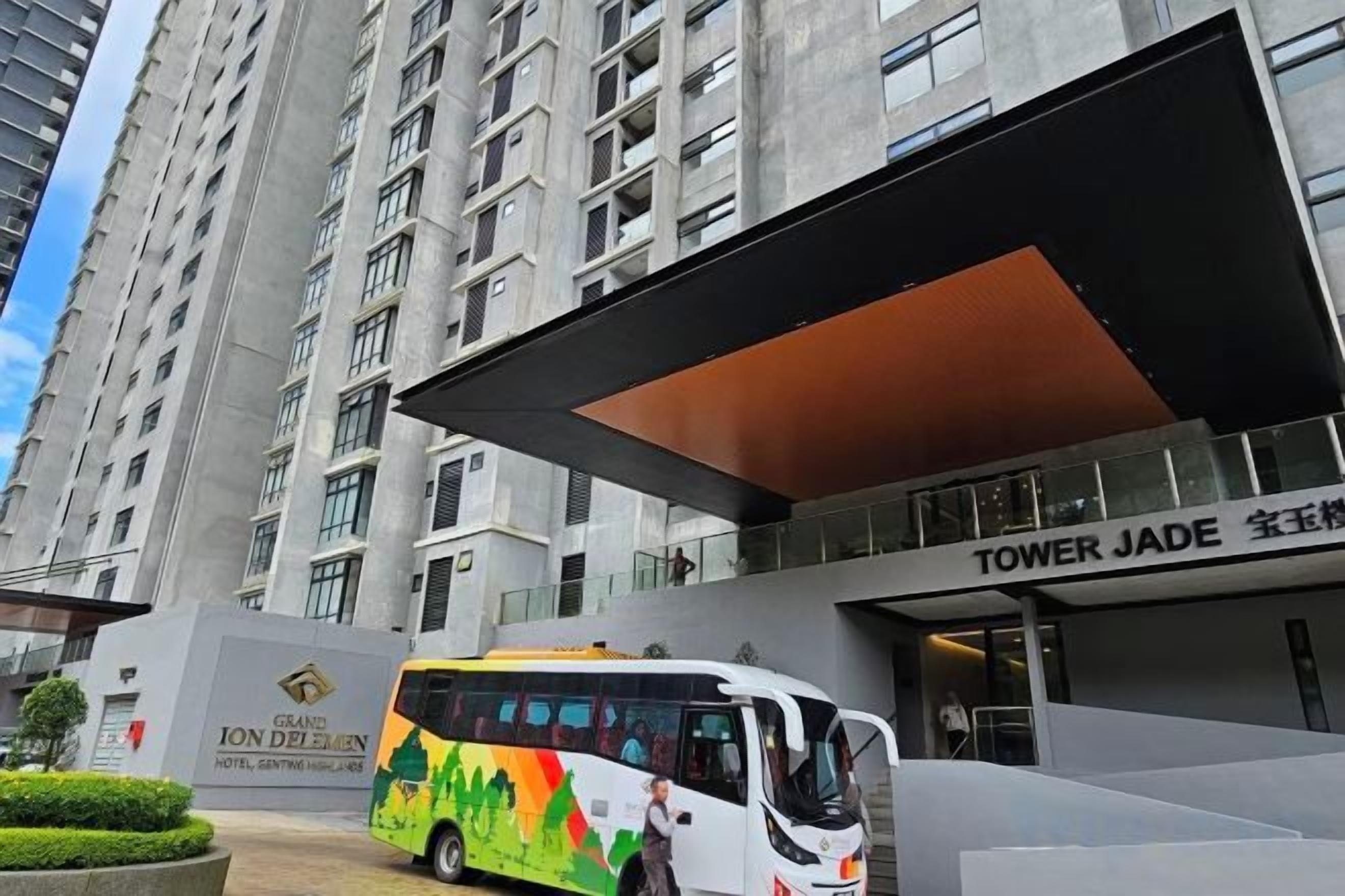 A modern hotel entrance with a bus parked in front, a large overhang, and a sign for 'TOWER JADE.'
