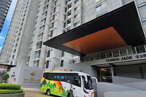 A modern hotel entrance with a bus parked in front, a large overhang, and a sign for 'TOWER JADE.'