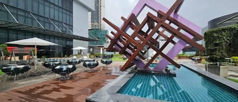 Ein Poolbereich im Freien mit einer modernen Skulptur, Sitzgelegenheiten und einem Gebäude im Hintergrund.