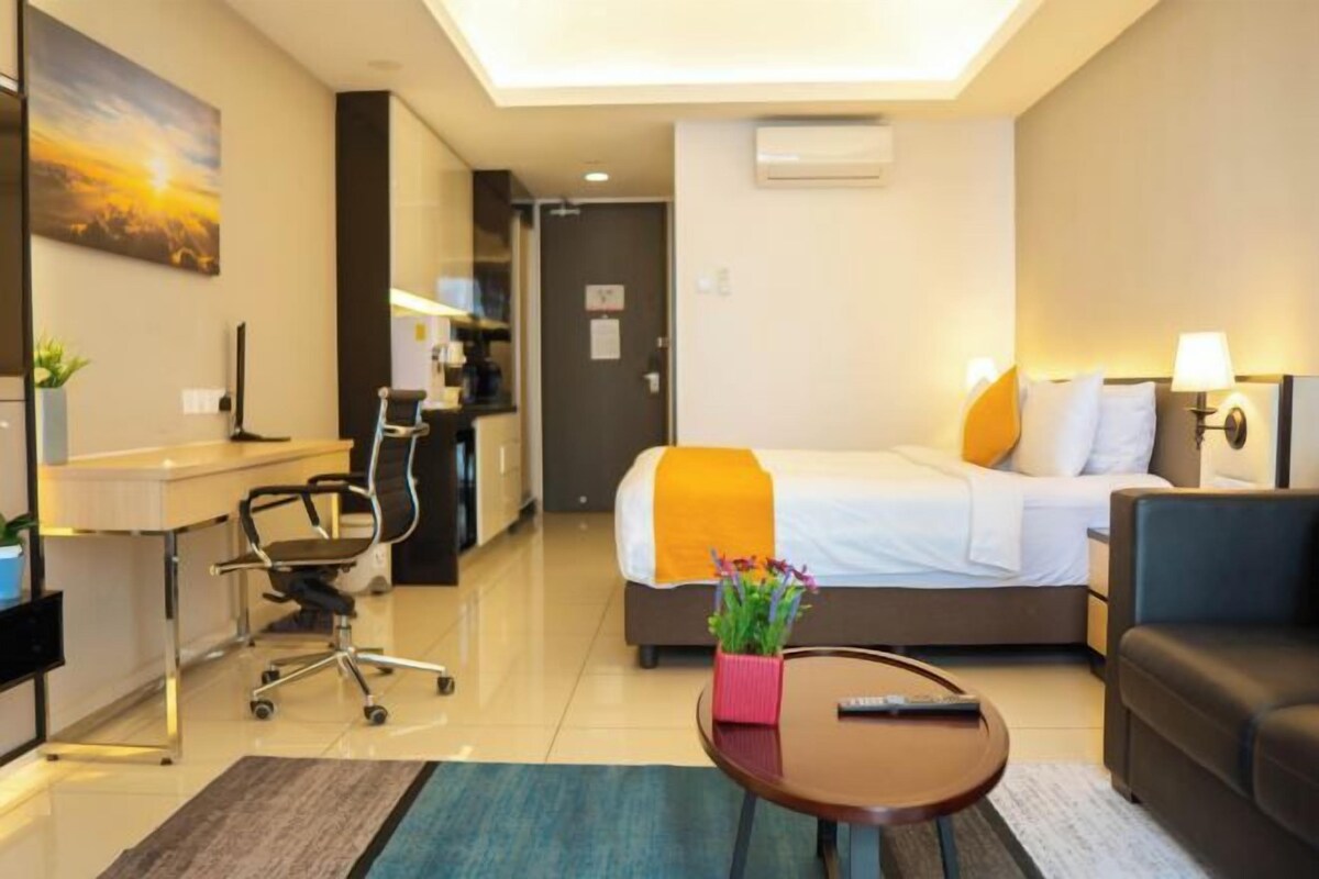 A hotel room with a bed, a desk, a chair, a sofa, and a small table with a vase of flowers.