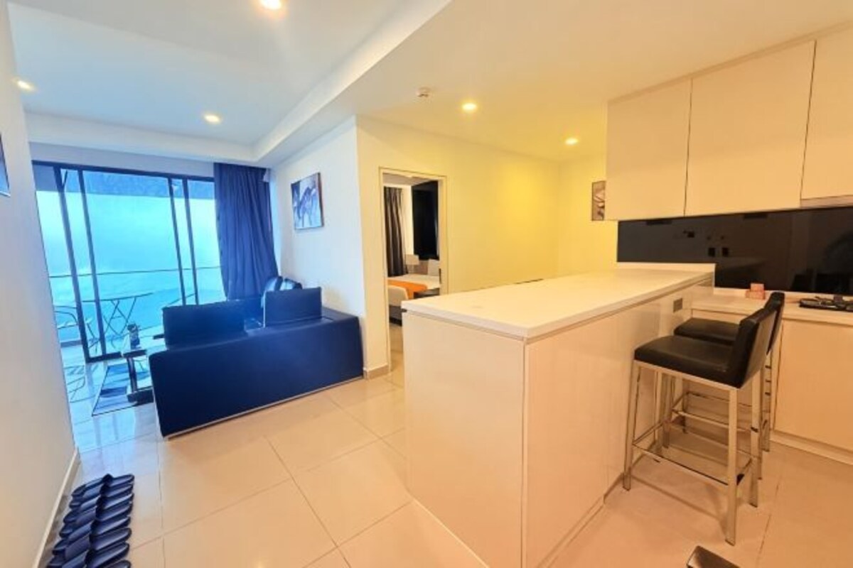 A modern kitchen with white cabinets, a bar area, and a view of the sea.
