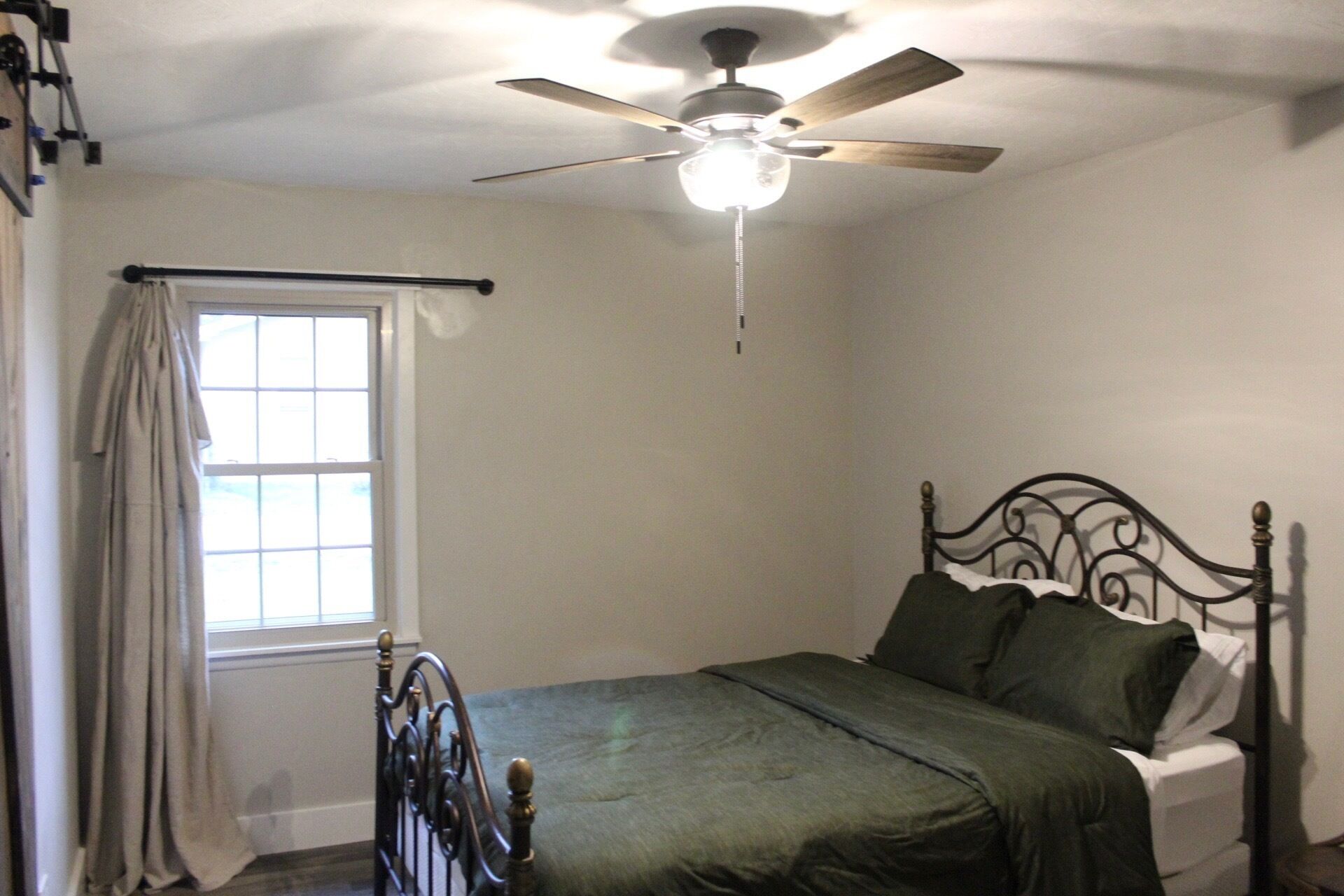 A bedroom with a single bed, a ceiling fan, and a window with curtains.