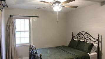 A bedroom with a single bed, a ceiling fan, and a window with curtains.