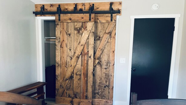 A room with a wooden barn-style sliding door, a dark door, and two wooden benches. - Snuggle up and relax with the whole family at this Ava home.  (Ava)