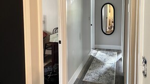 A hallway with a wooden floor, a rug, a mirror, and a door leading to another room. - Snuggle up and relax with the whole family at this Ava home.  (Ava)