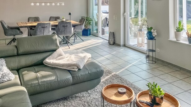 Una sala de estar moderna con un sofá gris, una mesa de comedor con sillas y un amplio ventanal corredera que da a un balcón.