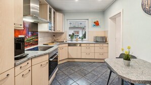 Una cocina moderna con horno integrado, microondas y lavavajillas. Se ve una ventana con vistas a una casa y plantas afuera.
