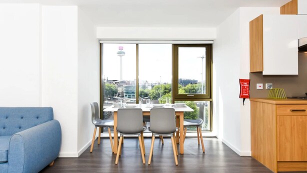 Ein modernes Wohnzimmer mit einem blauen Sofa, einem Esstisch mit vier Stühlen und einer Küchenzeile mit Holzschränken.