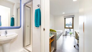 Ein modernes Hotelzimmer mit Bad, einem Bett, einem Schreibtisch und einem großen Fenster mit Blick auf die Stadt.