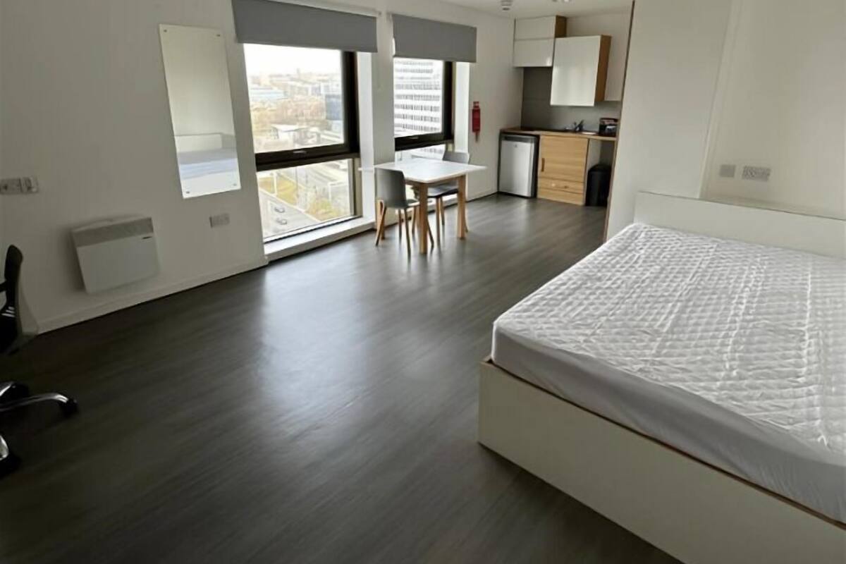 A modern bedroom with a large bed, a desk with a chair, and a kitchenette.