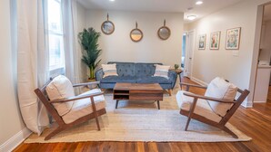 Ein Wohnzimmer mit einem blauen Sofa, zwei Holzstühlen, einem Couchtisch und einer großen Pflanze.