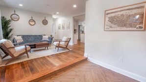 Ein geräumiges Wohnzimmer mit grauem Sofa, einem Holztisch und zwei Sesseln. An der Wand hängt eine große, gerahmte Karte.