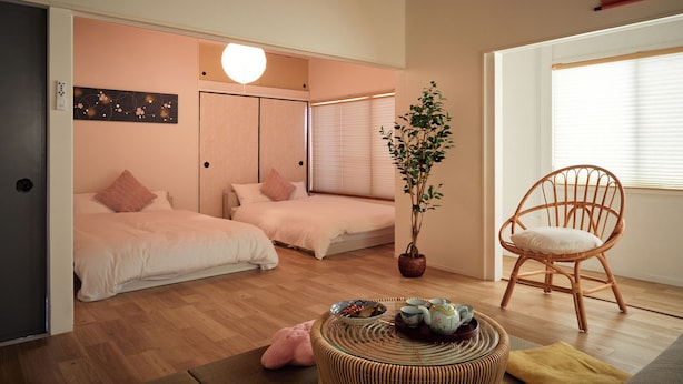 Un dormitorio acogedor con dos camas, una planta en maceta, un sillón de mimbre y una mesita con tazas y cuencos.