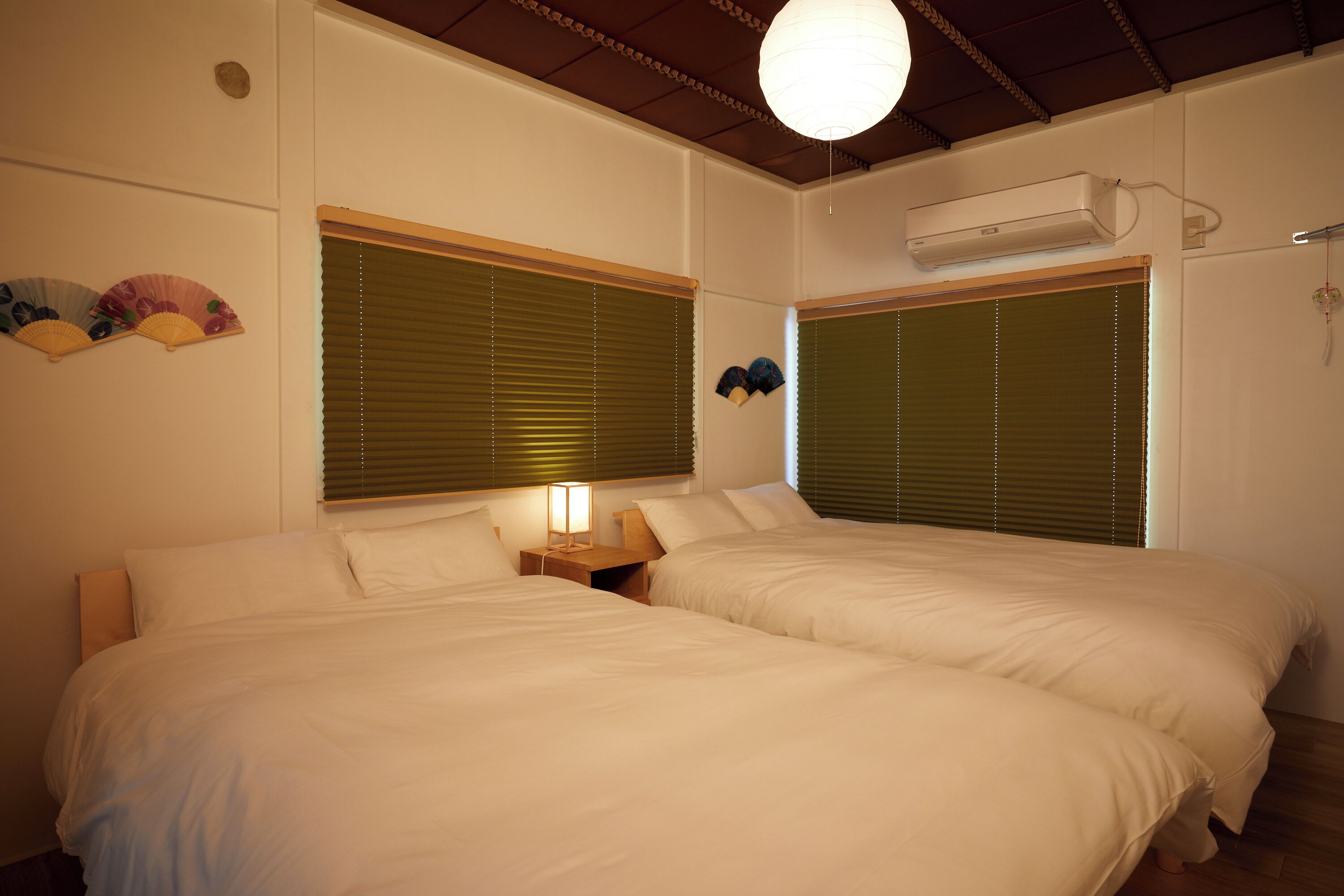 A room with two beds, a bedside table with a lamp, and a ceiling fan.