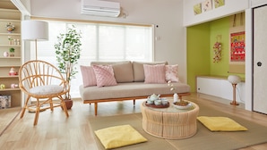 Una sala de estar con un sofá, una silla de mimbre, una mesita redonda y una planta en maceta.