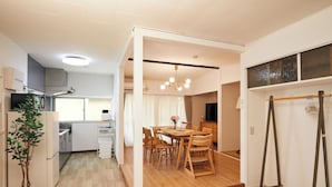 Una cocina moderna con armarios blancos, horno empotrado y refrigerador. Cuenta con una zona de comedor con mesa y sillas de madera, y una lámpara colgante arriba.