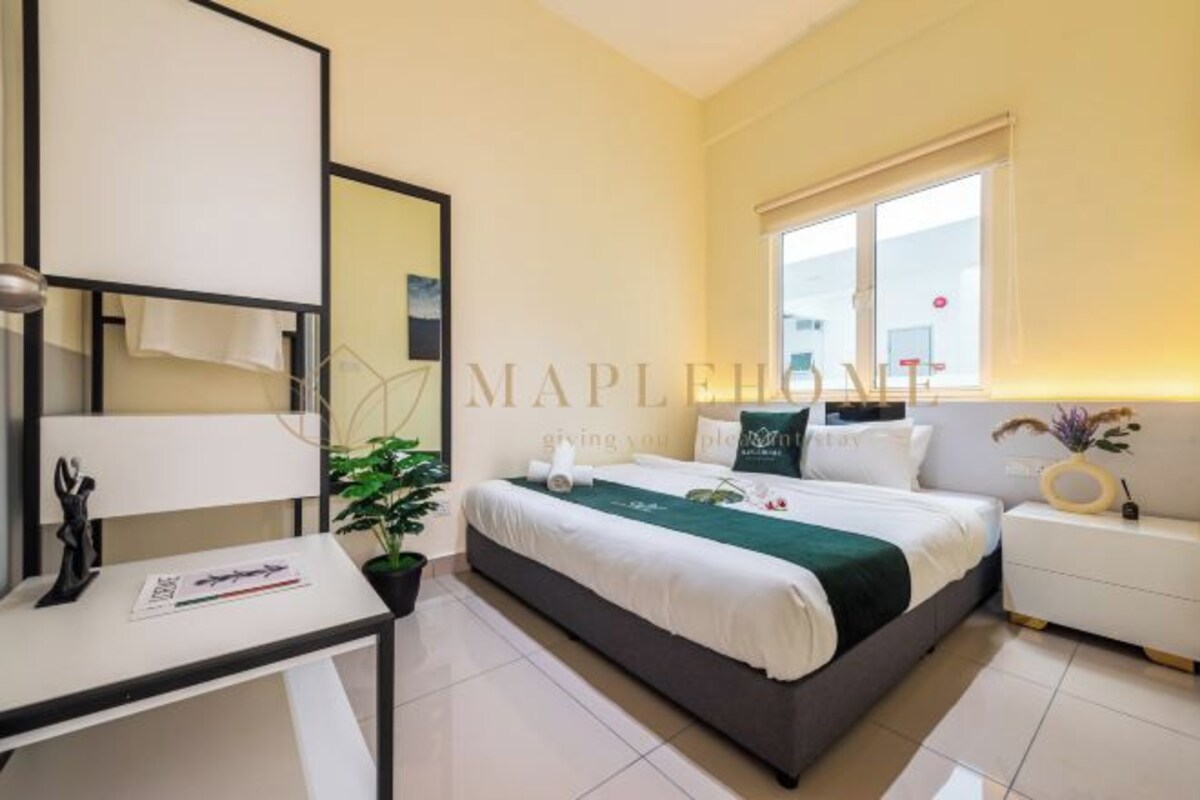 A bed with a white and green bedspread, a bedside table with a ring, and a white nightstand.