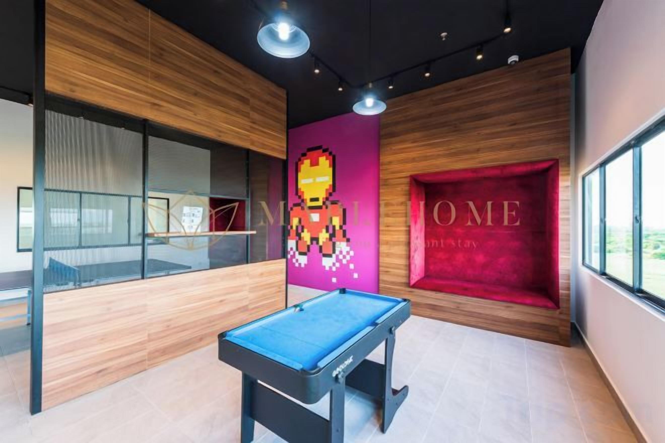 Una mesa de billar en una habitación con un ventanal grande, paneles de madera y una pared de acento roja con la palabra 'HOME' escrita.