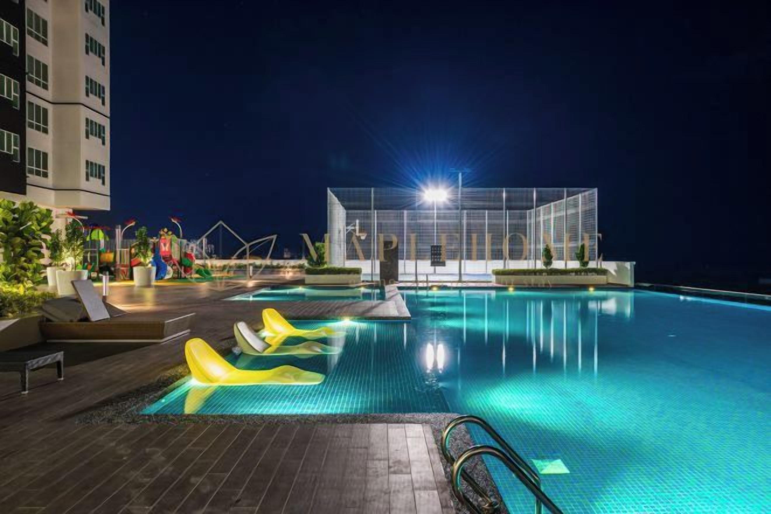 Zona de piscina por la noche con sillones de descanso y una estructura cubierta.