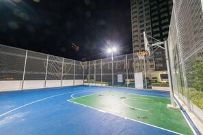 Una cancha de baloncesto al aire libre con aro, red y una valla alrededor.