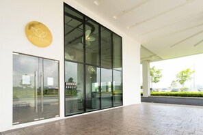 Una entrada moderna con puertas de vidrio, un logo visible y un espacio exterior cubierto.