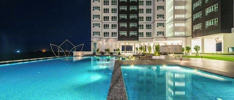 A swimming pool with a tiled edge, surrounded by a building with multiple floors and windows.
