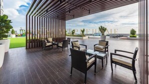 An outdoor seating area with wooden flooring, cushioned chairs, and a view of the sea. - Amber Cove Premier Suites Melaka (Melaka)