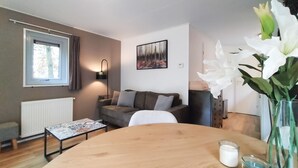 En hyggelig stue med sofa, sofabord, et billede på væggen og et vindue med gardiner.