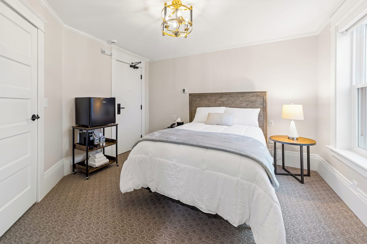 Ein Hotelzimmer mit einem großen Bett, einem kleinen Nachttisch mit Lampe, einem Fernseher auf einem Schrank und einem Kleiderschrank.