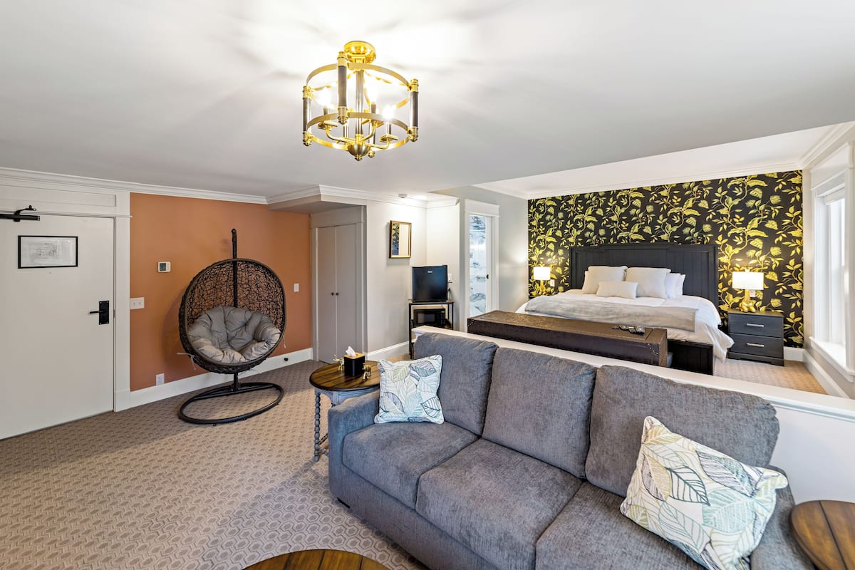 Ein Schlafzimmer mit einem Bett, einem grauen Sofa, einem Hängesessel und einer Chandelier.
