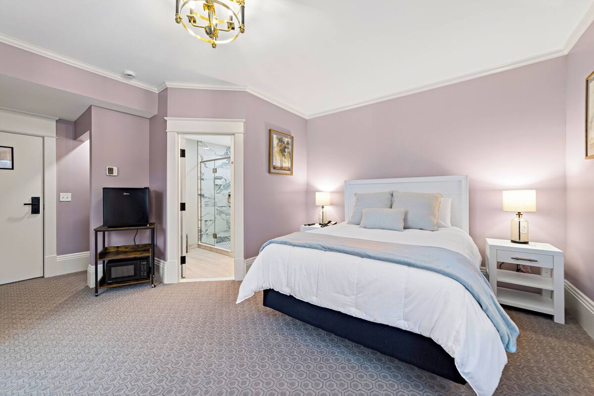 Ein Schlafzimmer mit Bett, Nachttischen, einem Fernsehtisch und einer Tür zu einem Badezimmer.