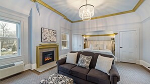 A bedroom with a fireplace, a large bed, a sofa, and a patterned ottoman. - The White Inn (Fredonia)