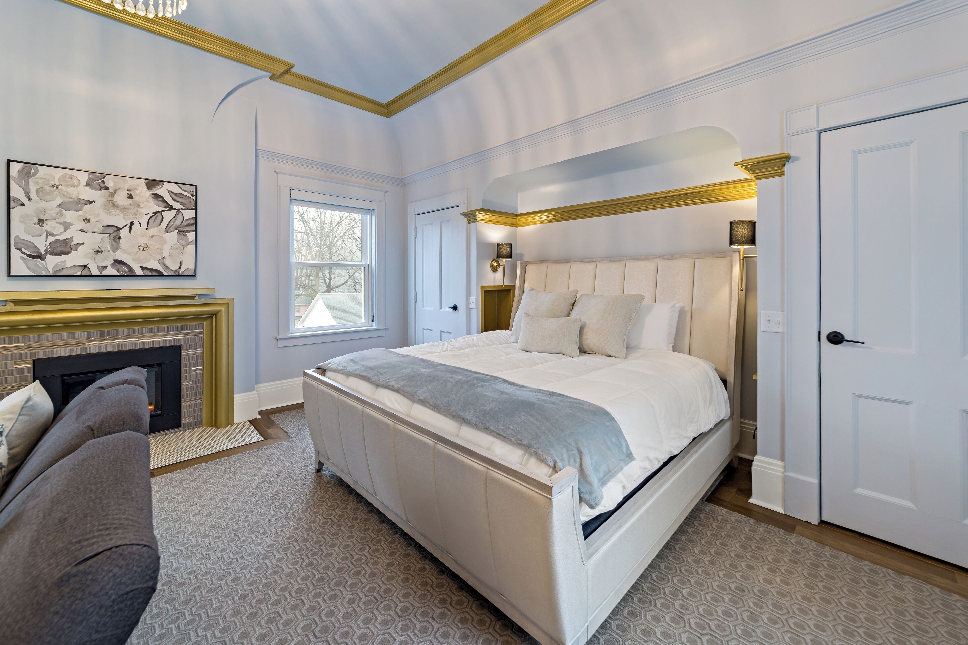 A bedroom with a large bed, a fireplace, a sofa, and a door.