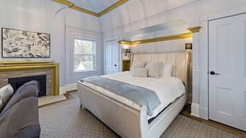 A bedroom with a large bed, a fireplace, a sofa, and a door.