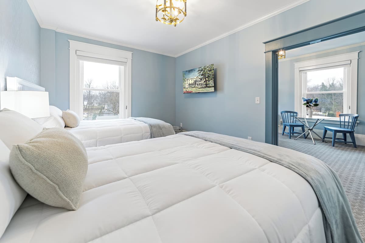 Ein Schlafzimmer mit zwei Betten, einer Essecke mit blauen Stühlen und einem Kronleuchter.