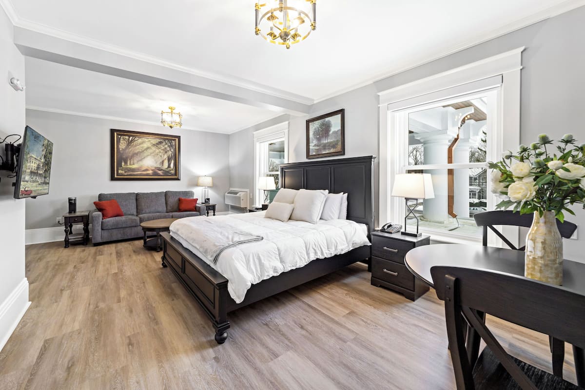 Ein Schlafzimmer mit einem großen Bett, einer Couch, einem Schreibtisch und einem Sessel. An den Wänden befinden sich Gemälde und es hängt ein Kronleuchter.