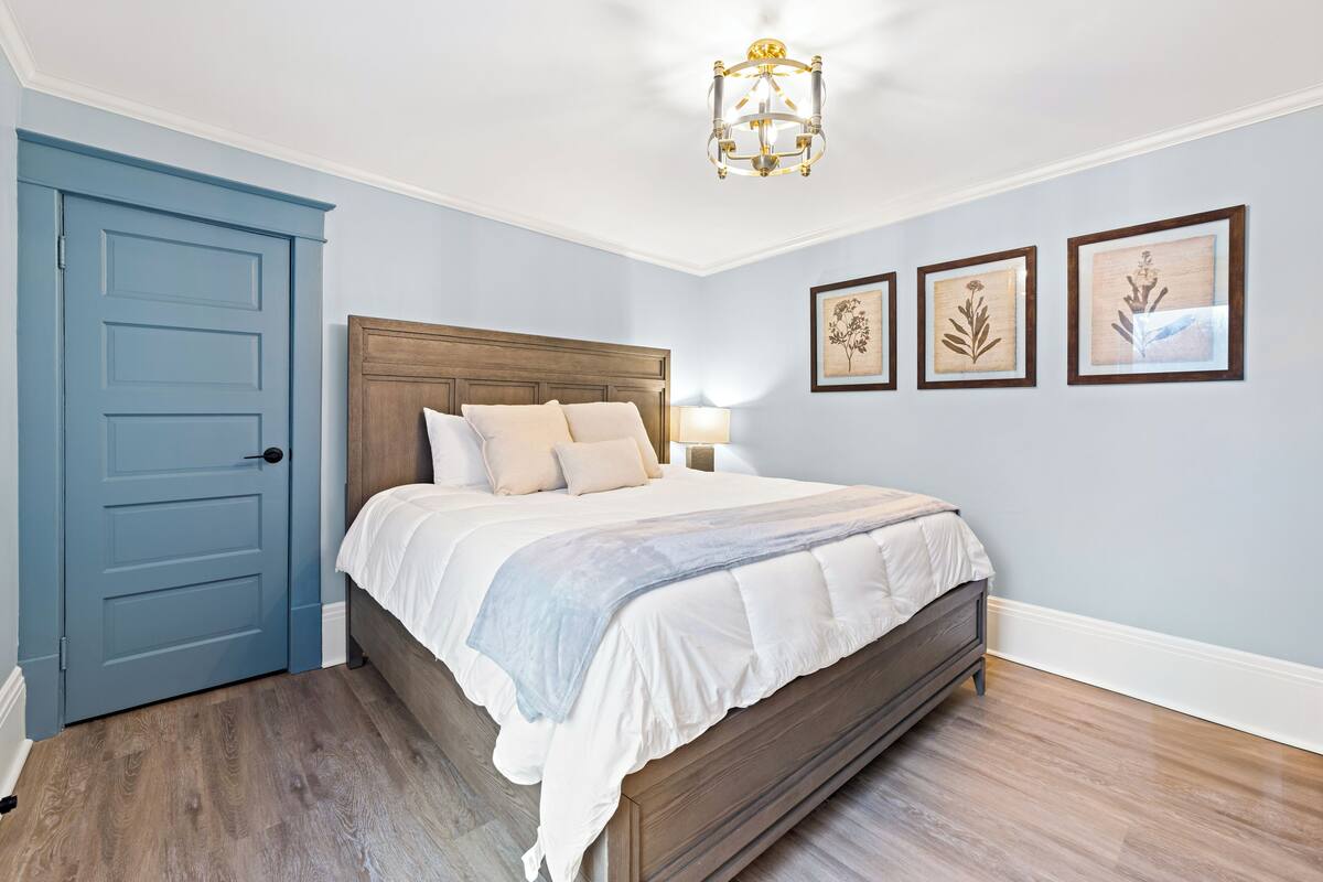 Ein Schlafzimmer mit einem hölzernen Bett, einer blauen Tür und drei gerahmten Pflanzenbildern an der Wand.