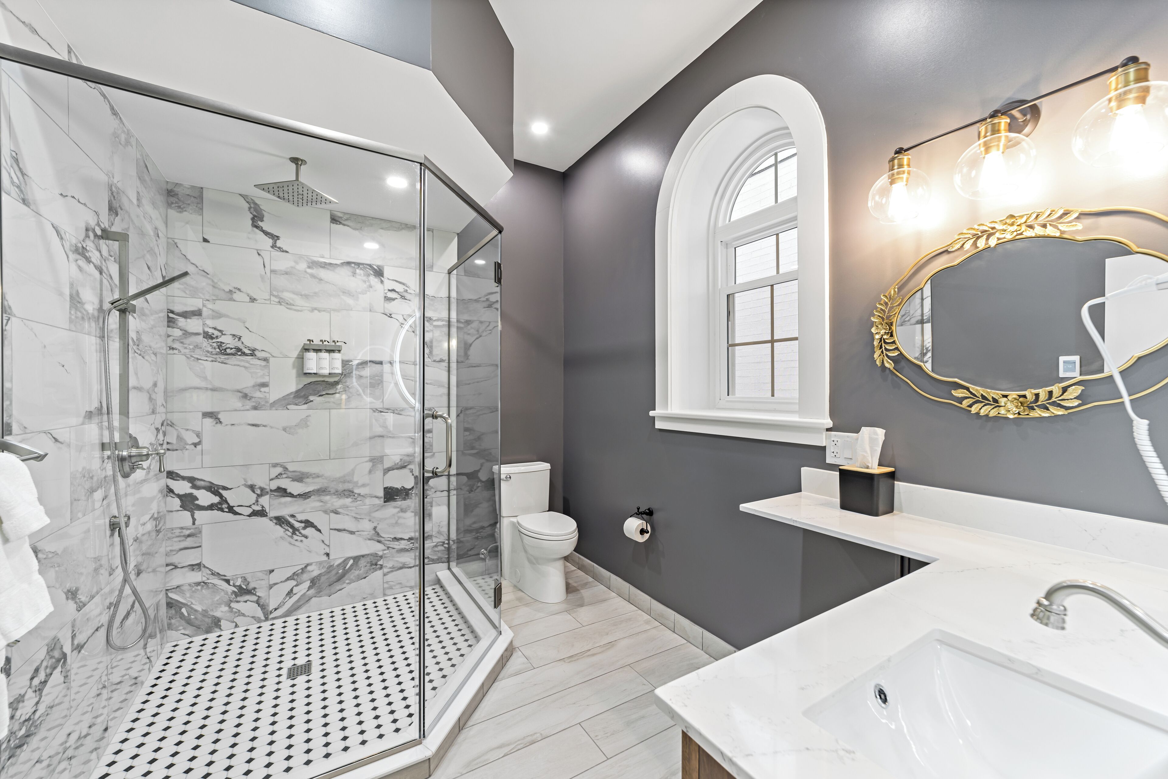 Un bagno moderno con cabina doccia in vetro, lavandino bianco e mobile contenitore con specchio dalla cornice dorata.