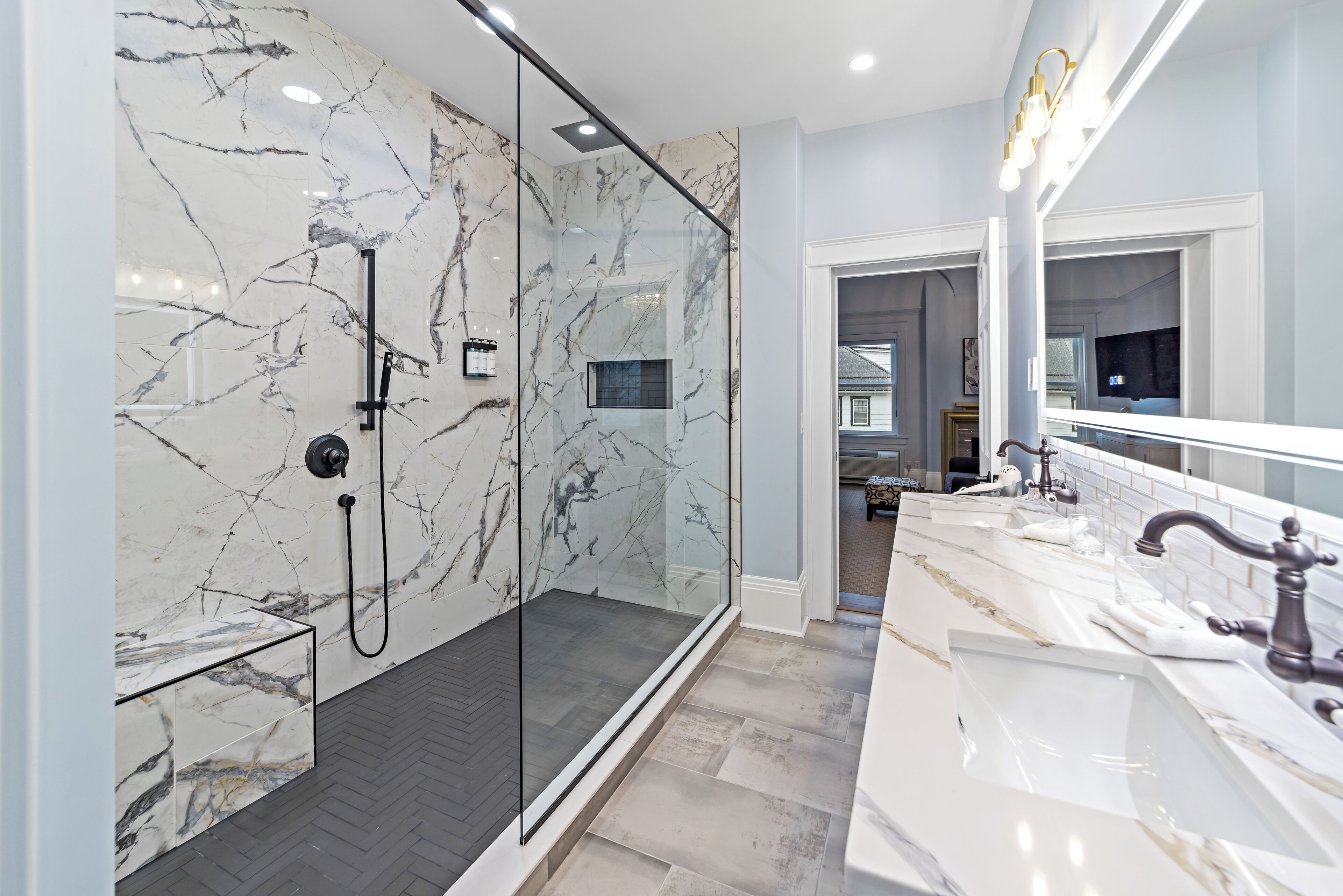 Une salle de bain moderne avec une douche à parois de verre, des murs en marbre et un grand miroir.
